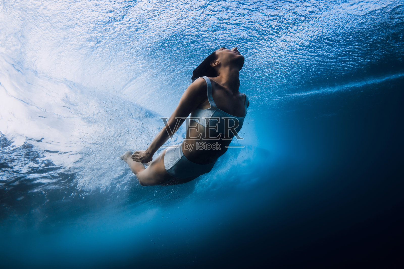冲浪女孩在海浪中潜水。没有冲浪板的桶状波浪下鸭式潜水照片摄影图片