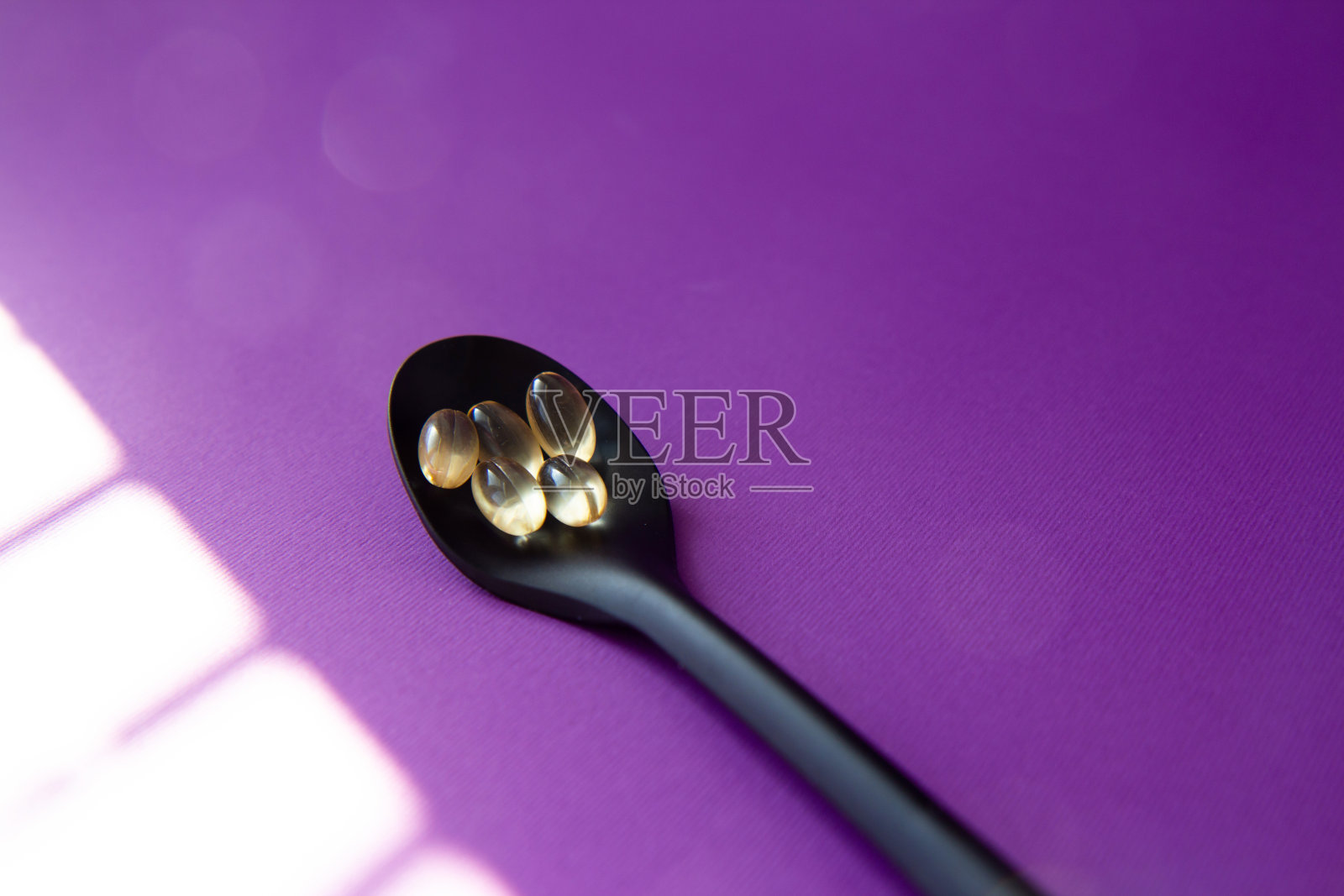 膳食补充剂。紫色背景的黑色勺子上的维生素片照片摄影图片