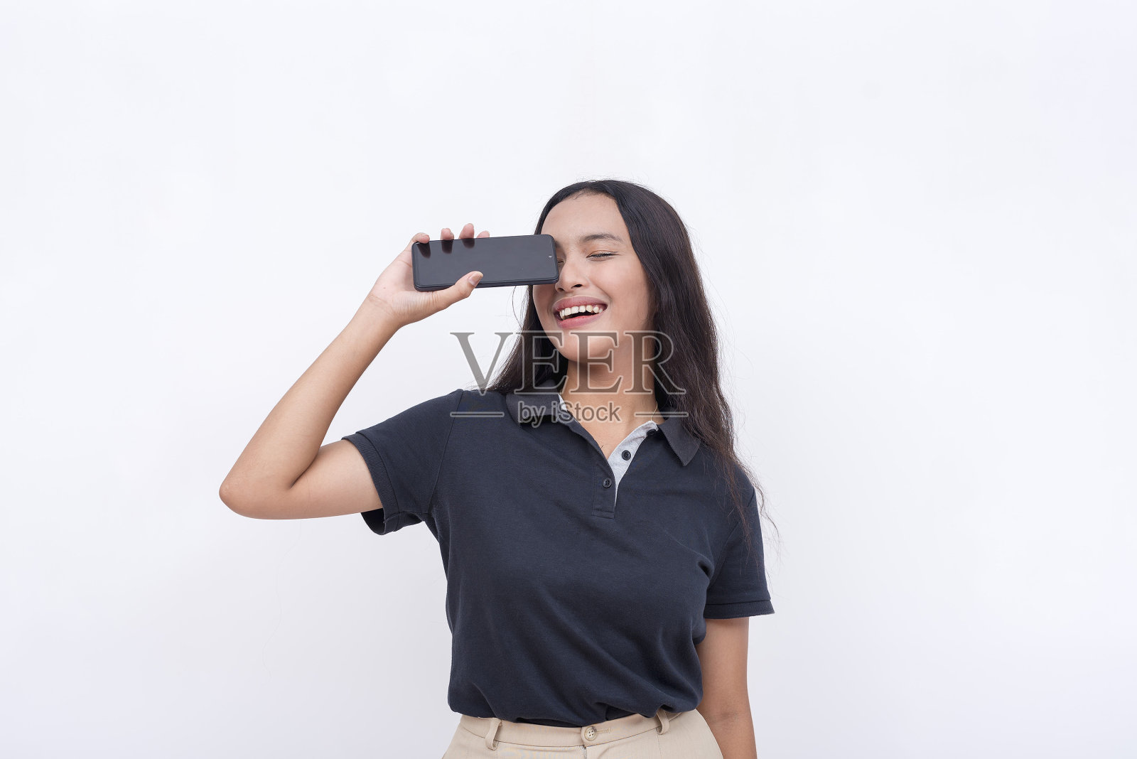 一个年轻幸福的亚洲女人水平拿着手机，微笑着。手机应用广告布局。照片摄影图片