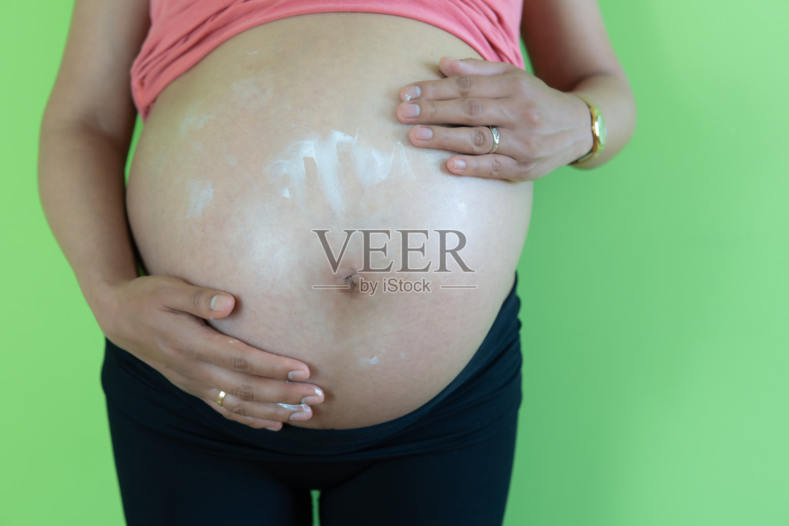 孕妇在腹部涂抹妊娠纹霜。怀孕，人和生育的概念。孕妇在腹部绿色背景上涂抹抗妊娠纹霜照片摄影图片