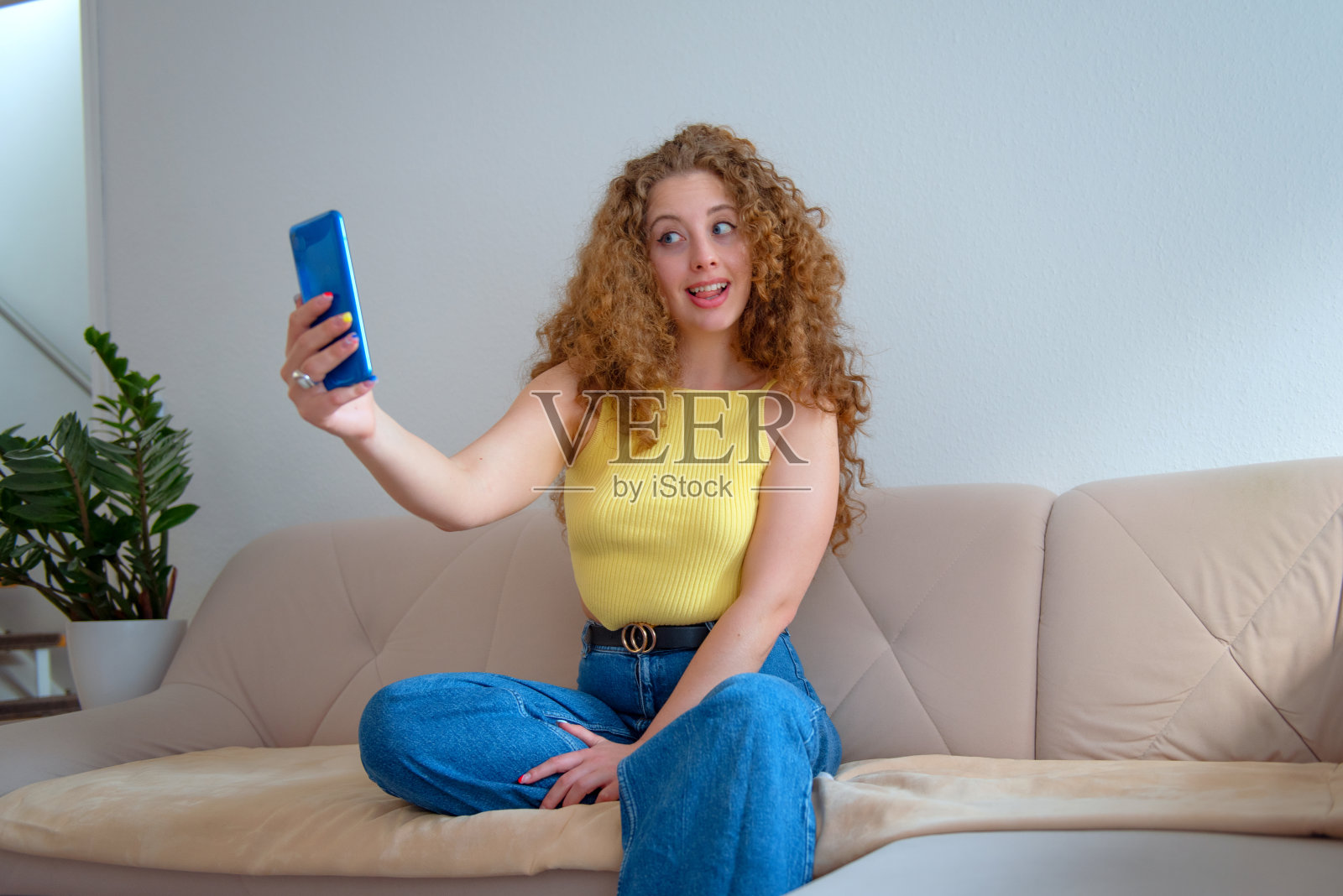 一个美丽开朗的卷发女人坐在家里的沙发上玩手机的画像照片摄影图片