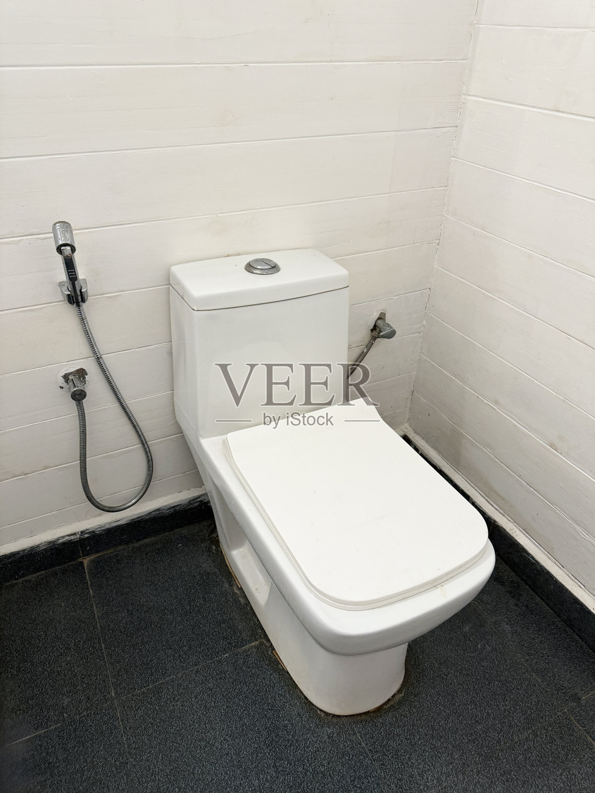 浴室的特写图像，灰色的瓷砖地板，白色的紧密耦合厕所(水箱附碗)，手淋浴坐浴盆头附件，高架视图，重点在前景照片摄影图片