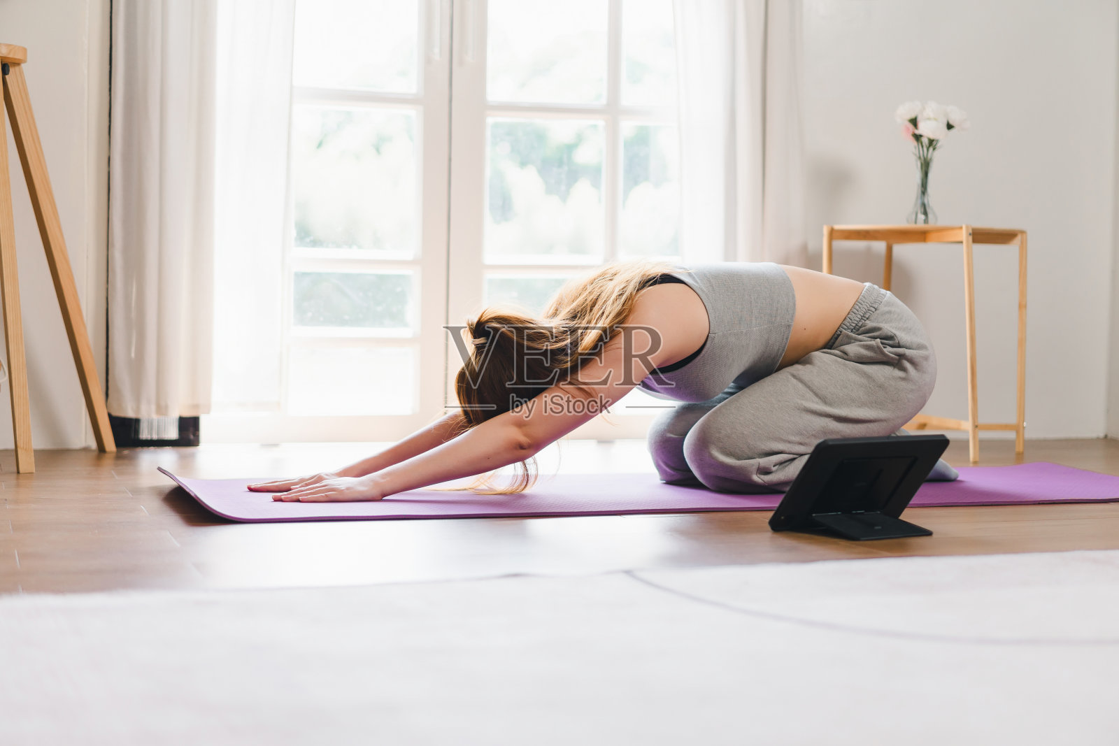 年轻的亚洲女性在家里对着打开的笔记本电脑做瑜伽，重复着专业在线健身教练的指导。照片摄影图片