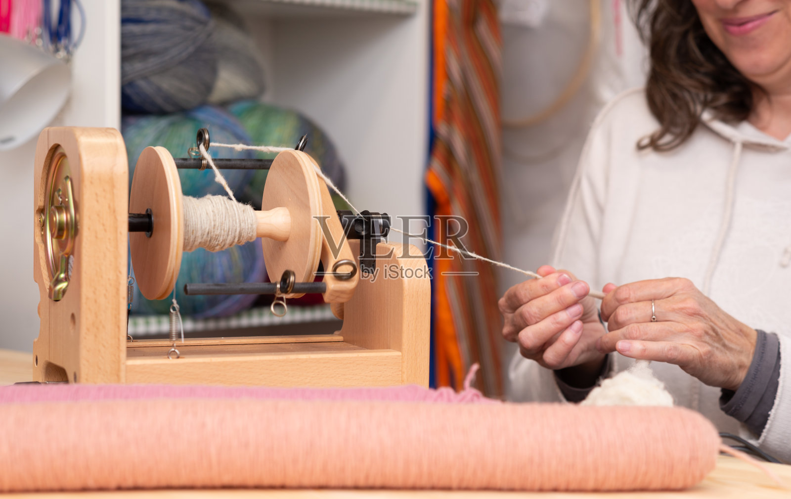 一个女手艺人在她的针织店里用电动纺车纺羊毛的特写。照片摄影图片