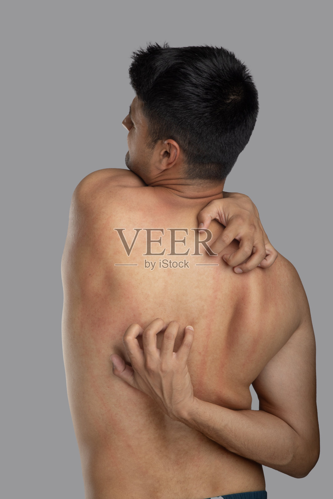 光膀子的年轻人在灰色的背景上搔痒照片摄影图片