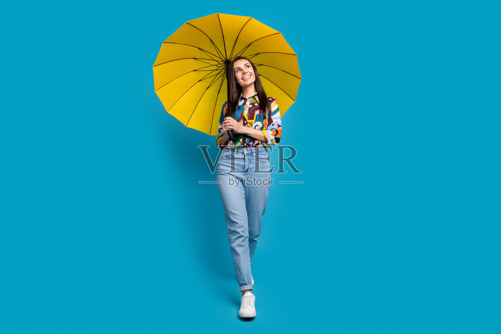 华丽的女人穿着印花衬衫牛仔裤的全长照片，拿着伞看销售空白空间孤立的蓝色背景照片摄影图片