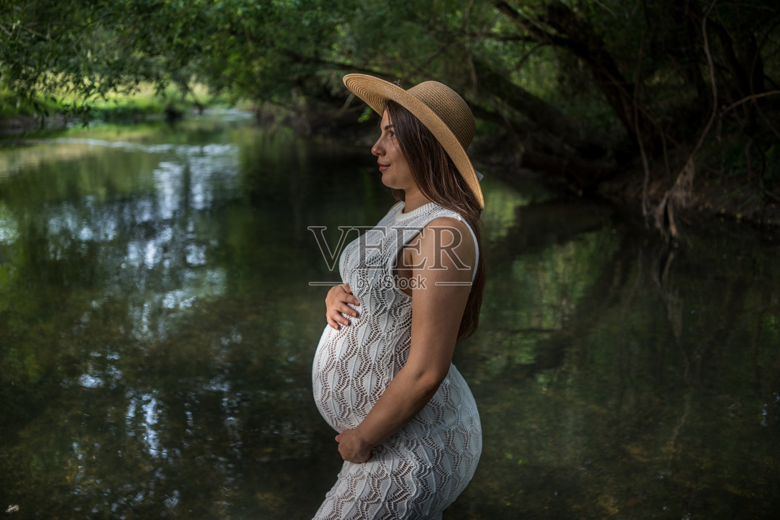 图为一名孕妇独自站在草地上，抚摸着肚子，享受着平静的草地。照片摄影图片