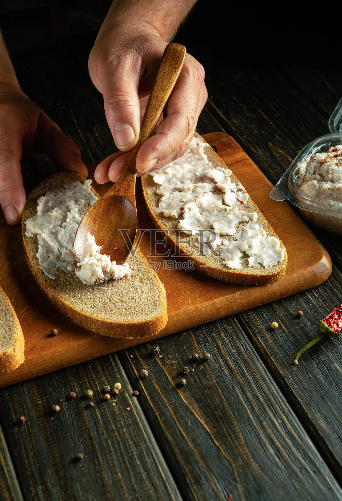 厨师用木勺将猪油涂抹在黑麦面包上，以便在厨房板上制作三明治。广告投放场所照片摄影图片