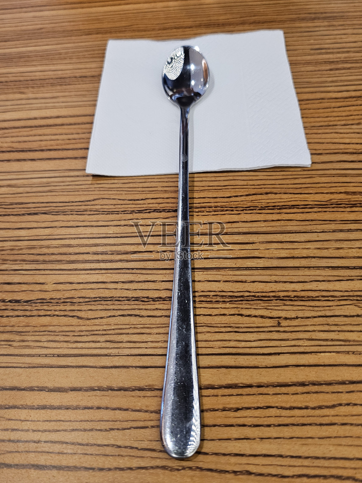 茶水用的铝勺放在纸巾上，放在木桌上。照片摄影图片