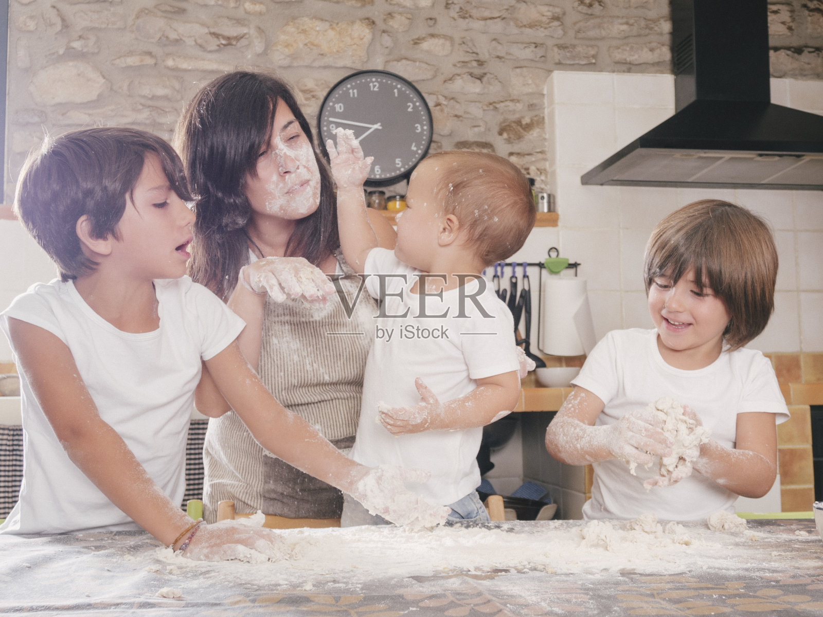 母亲在准备蛋糕时，脸上沾满了孩子们扔过来的面粉。厨房里的乐趣。照片摄影图片