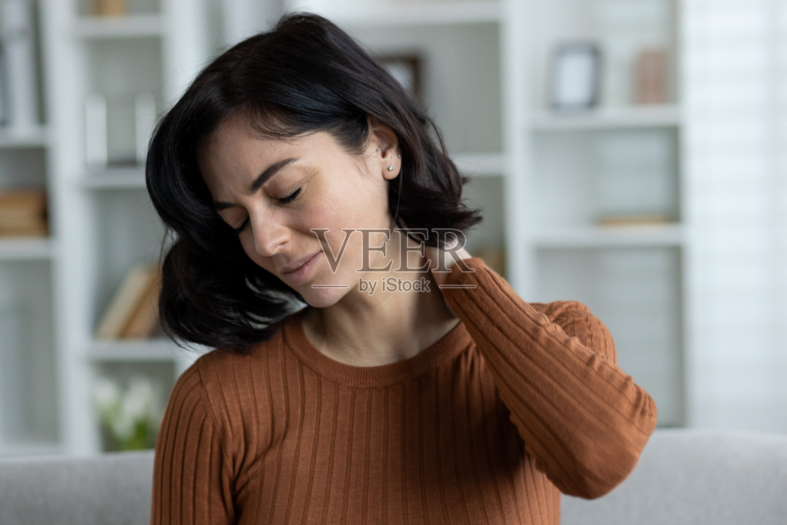 一张特写照片，一个年轻女子坐在家里的沙发上，痛苦地做着鬼脸，用手掐着脖子照片摄影图片