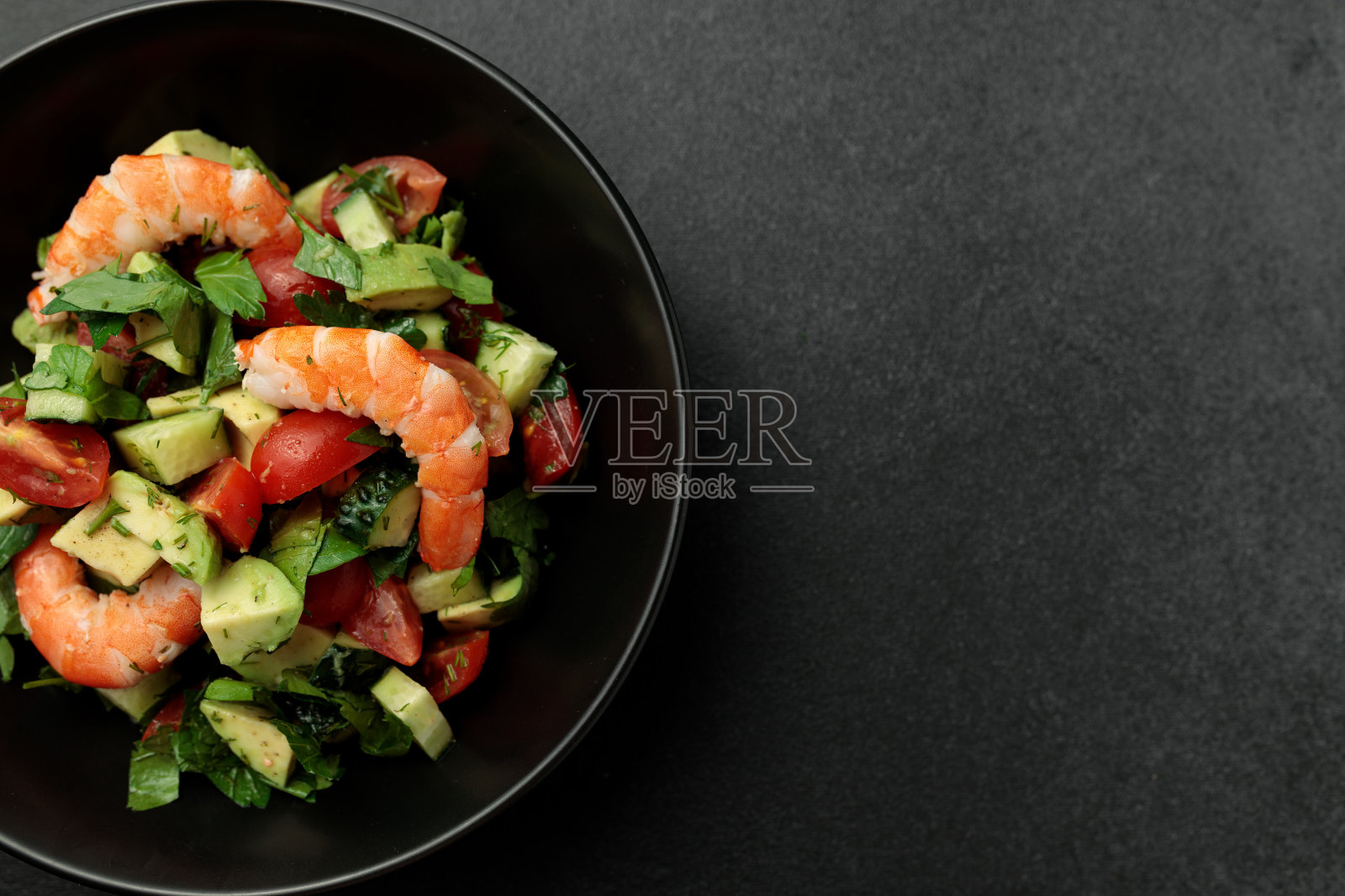 大虾沙拉，牛油果，黄瓜，番茄和香草。黑色背景照片摄影图片