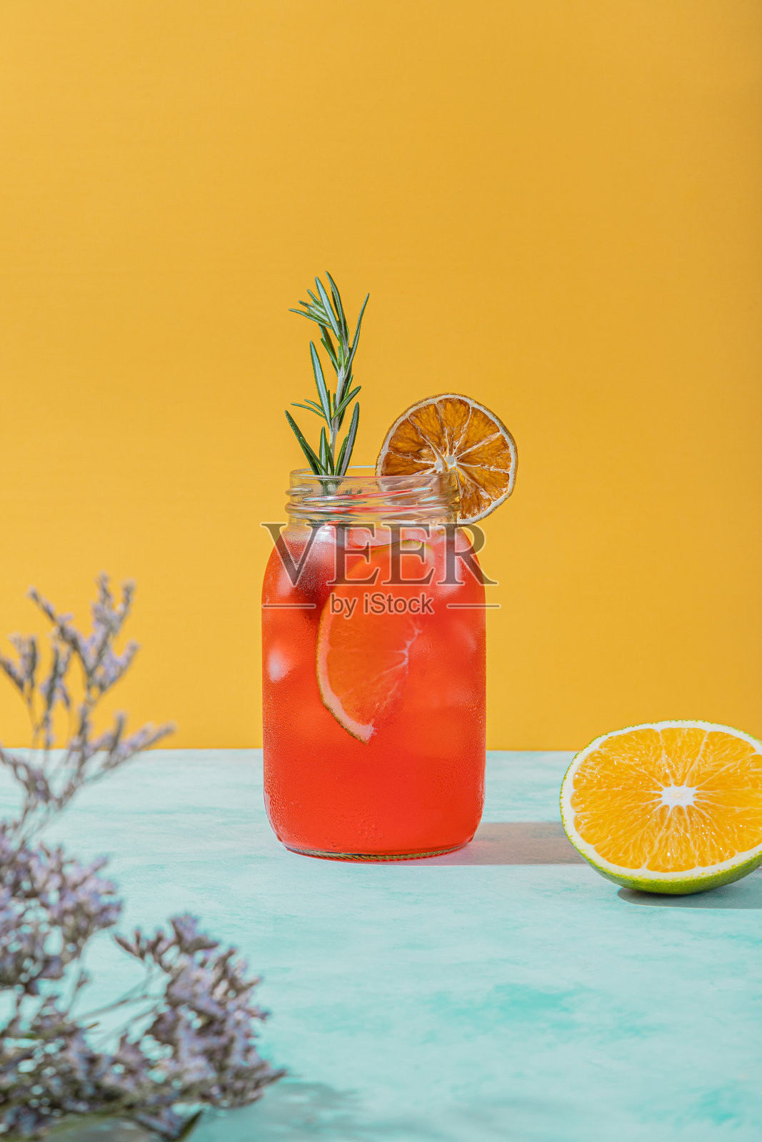 清爽的红色夏季鸡尾酒，在充满活力的黄色背景上点缀着橘子片和迷迭香照片摄影图片