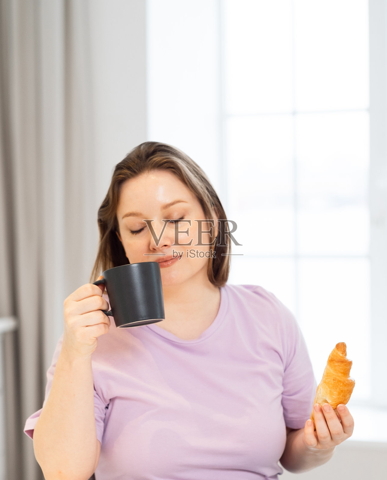 清晨在厨房里喝着咖啡吃着羊角面包的迷人曲线女人。照片摄影图片