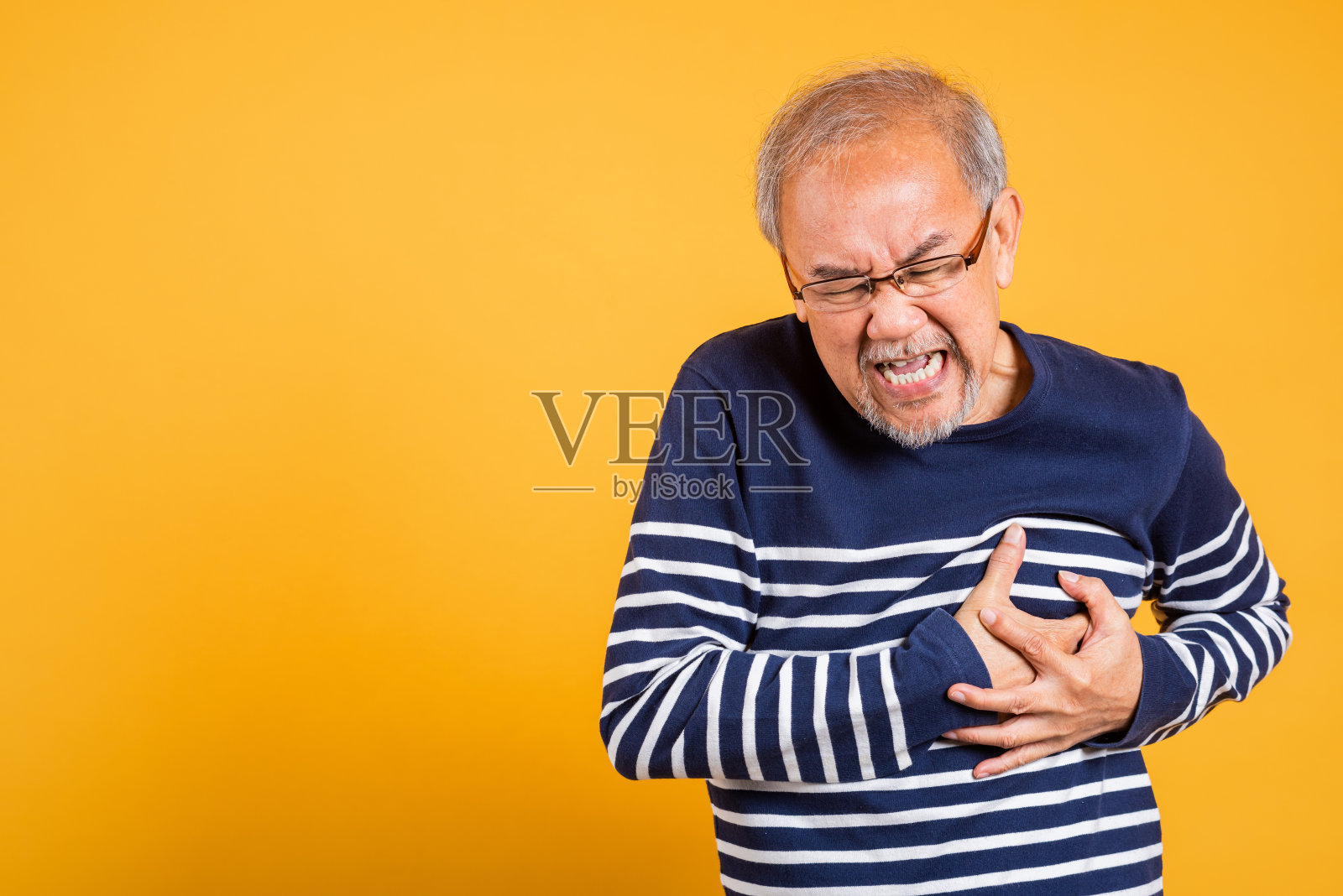 肖像亚洲老人戴眼镜双手放在胸前摄影棚拍摄孤立的黄色背景，老人退休与白发心脏病的痛苦照片摄影图片