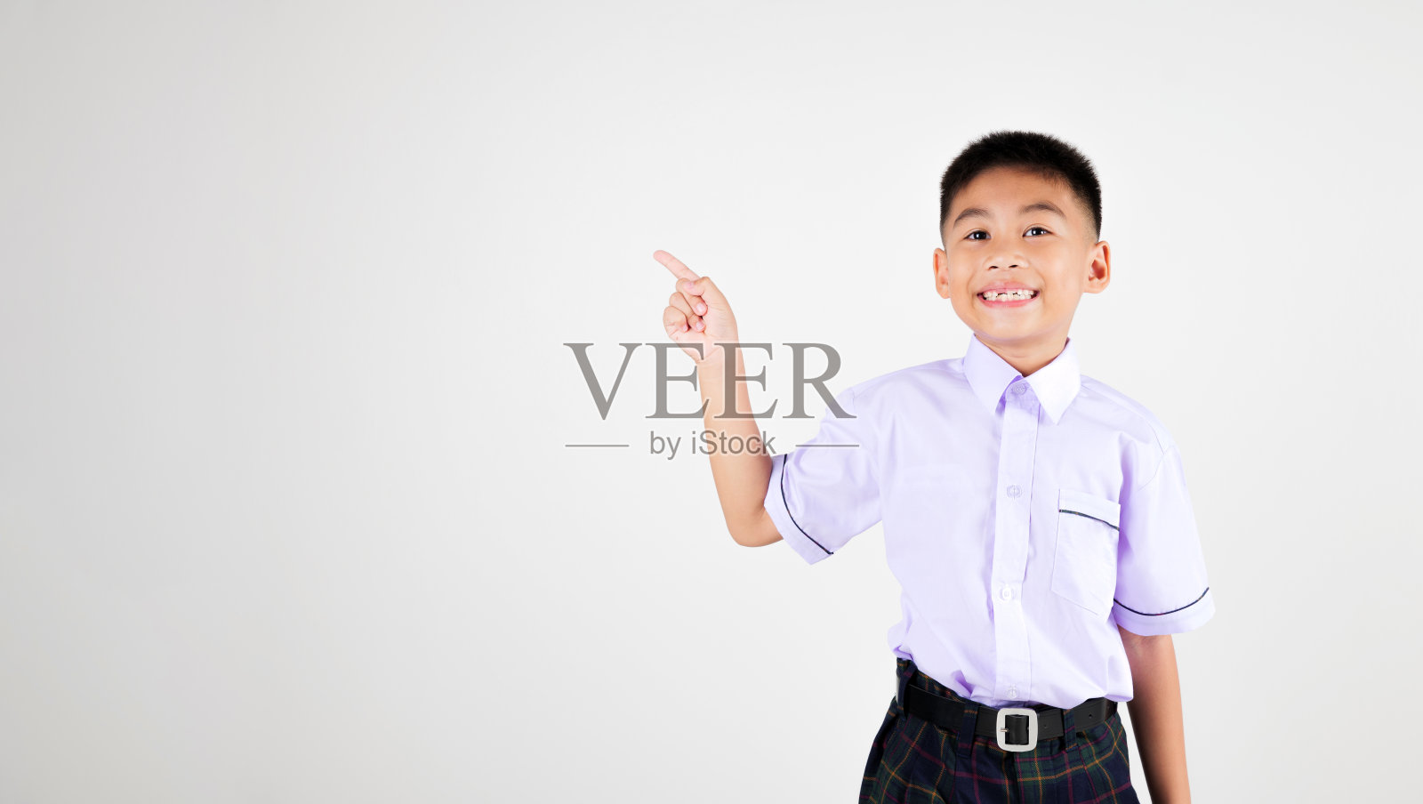 肖像微笑亚洲小男孩主要摆姿势，手指向一边撇去工作室孤立的白色背景，快乐可爱的男人孩子穿着校服格子的天真和好奇照片摄影图片