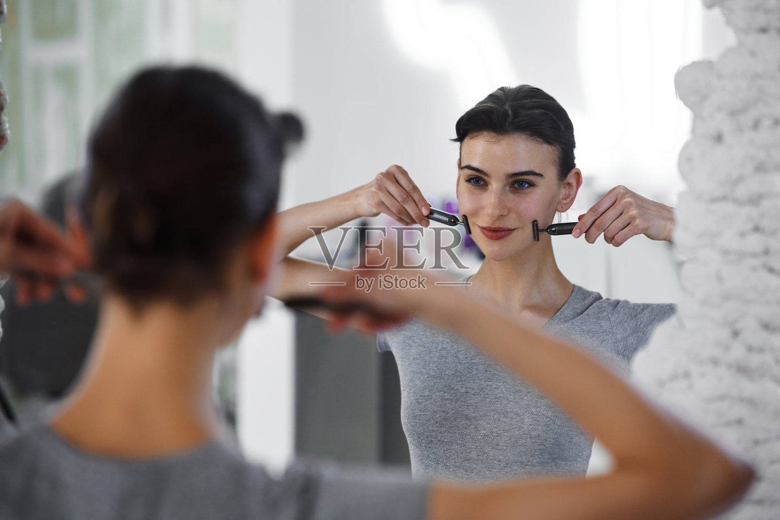 一位年轻女子一边照镜子，一边用水粉粉按摩脸部。照片摄影图片