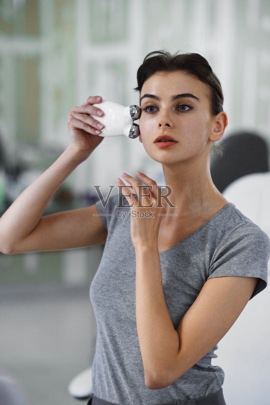 一位年轻女子一边照镜子，一边用微电流装置按摩脸部。照片摄影图片