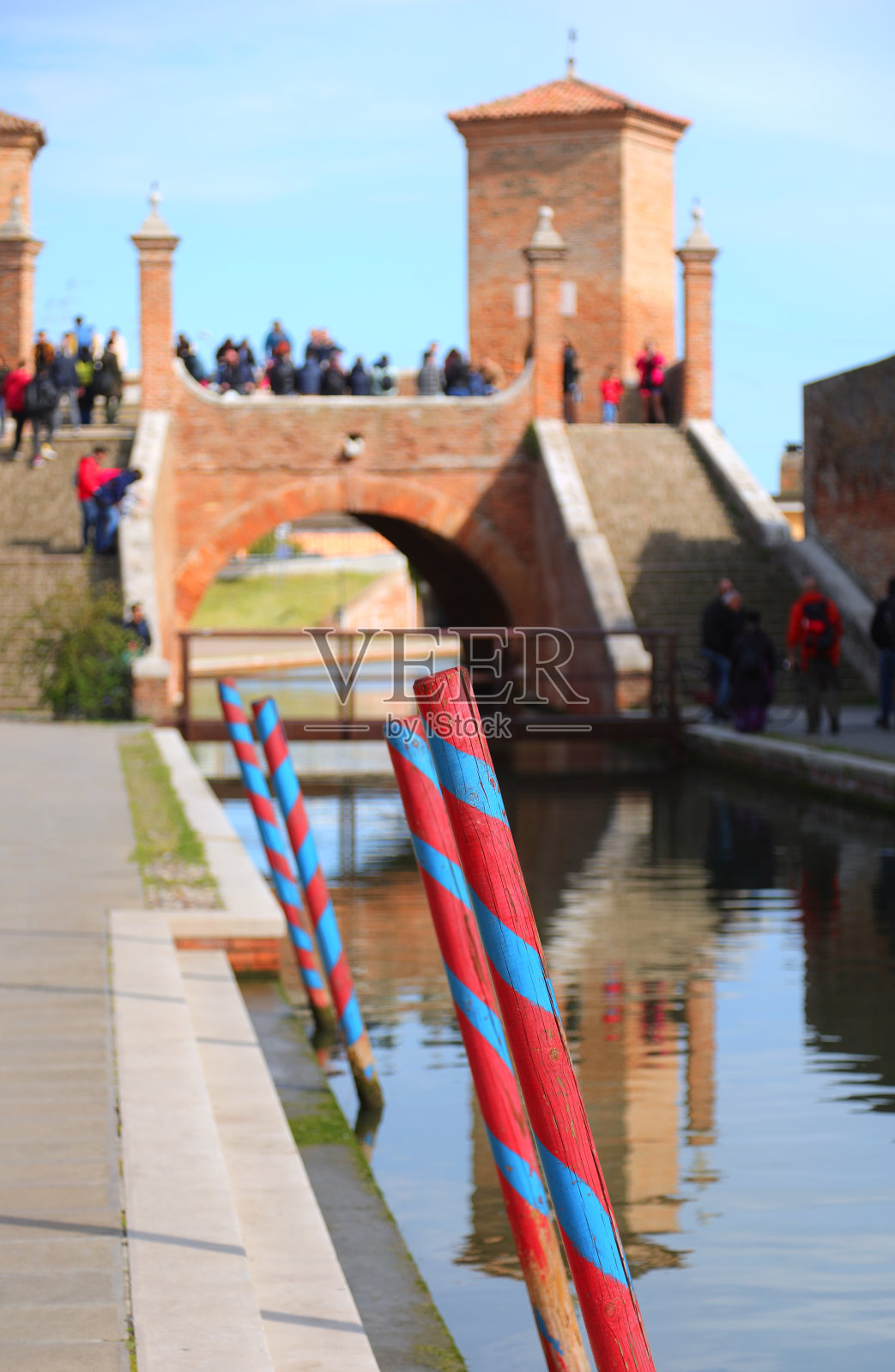 在运河中系泊船只的木杆和意大利著名的科马乔桥照片摄影图片