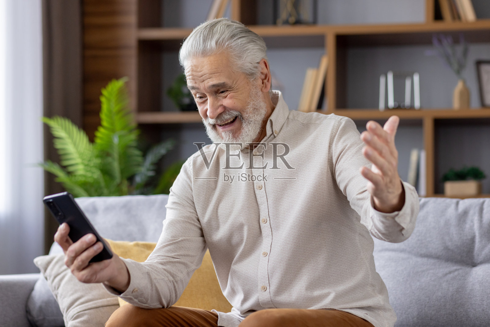 面带微笑的白发老人爷爷在电话里讲视频电话，坐在家里的沙发上开心地听到这个消息照片摄影图片