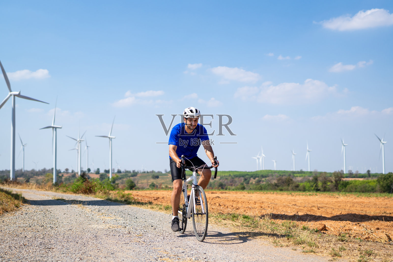 在风力涡轮机场骑自行车的高加索运动健将。有吸引力的运动员在运动服锻炼骑自行车锻炼户外健康和保健在农村地区风车发电厂。照片摄影图片