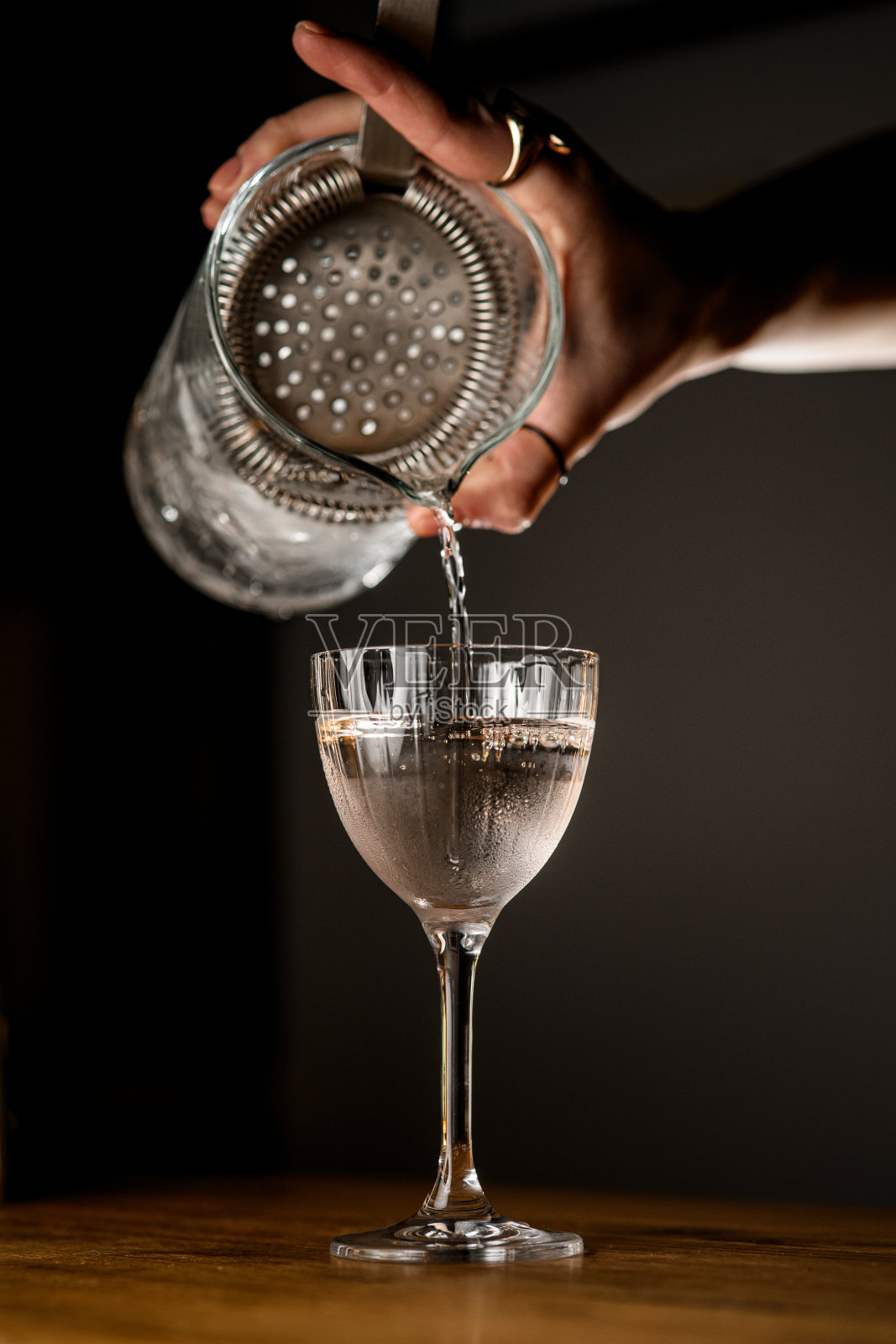 调酒师用女性的手从加冰的调酒杯中倒入清澈的饮料照片摄影图片