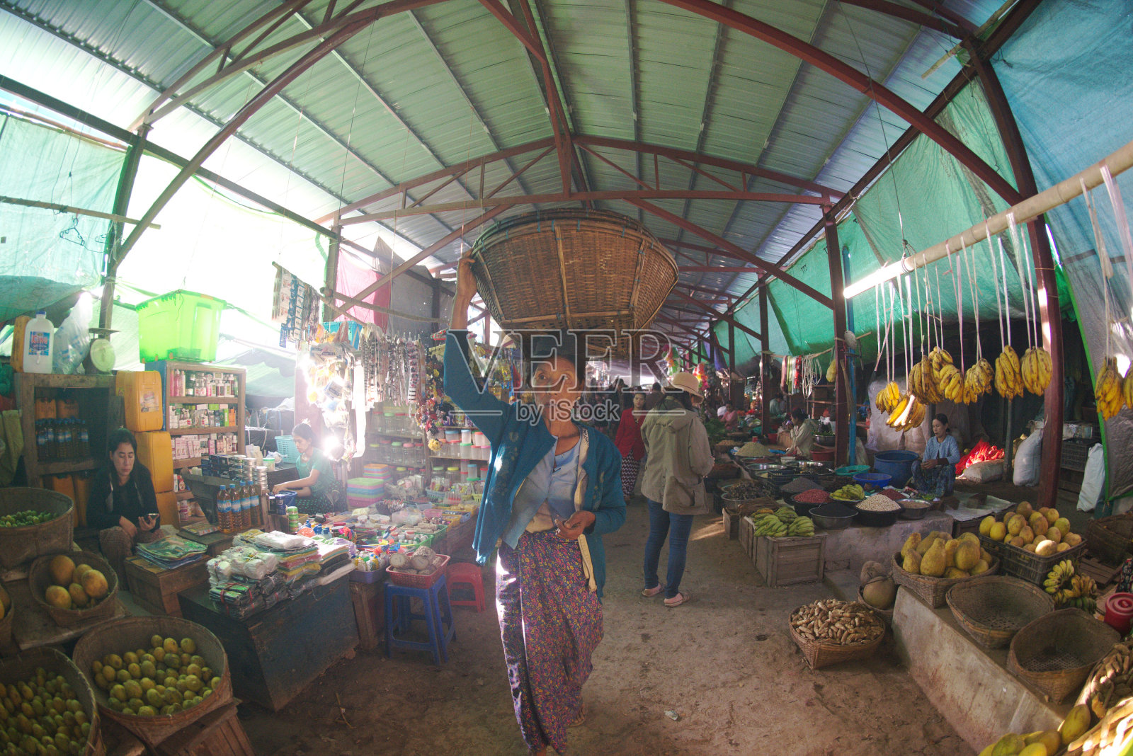 在早市，女商贩提着一篮子蔬菜或鲜花，把它顶在头上，带到她的摊位上。照片摄影图片