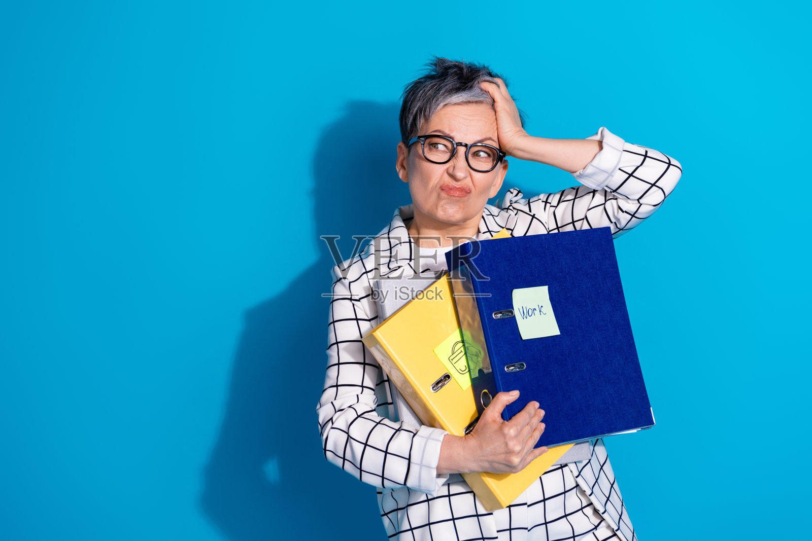 照片中，悲伤沮丧的退休妇女穿着白色西装，摸着头，在蓝色背景上看起来空空荡荡照片摄影图片