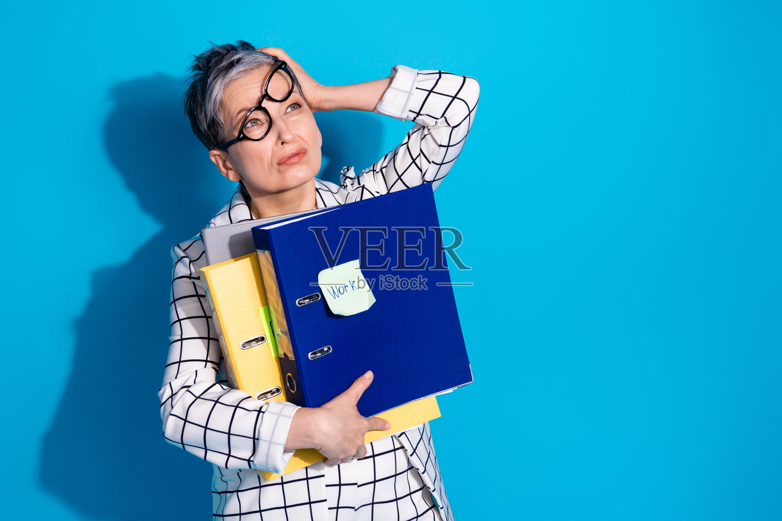 照片中，疲惫无聊的成功女性穿着白色时尚的衣服，拿着文件，在蓝色的背景上看起来空无一物照片摄影图片