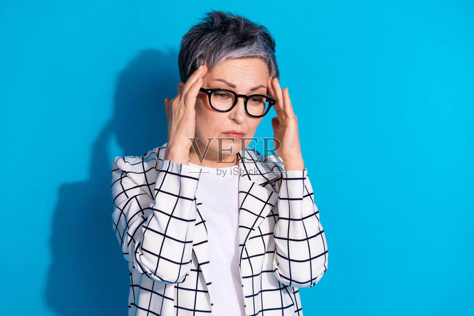 疲惫的退休妇女穿着白色时髦的衣服，在蓝色的背景上遭受痛苦的紧张照片摄影图片