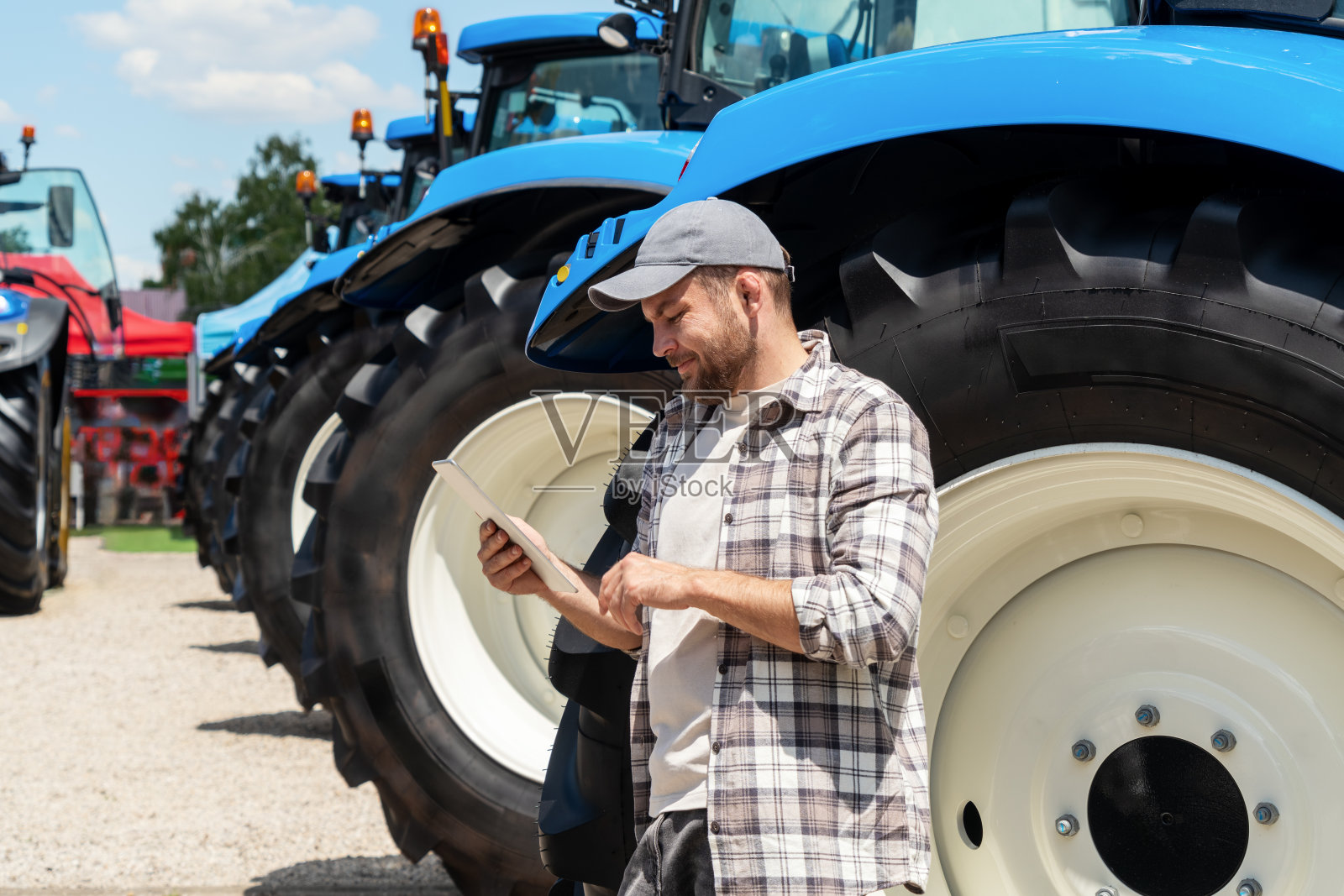 在农业机械经销店，一名农民站在新型农用拖拉机旁边，正在使用数码平板电脑。照片摄影图片