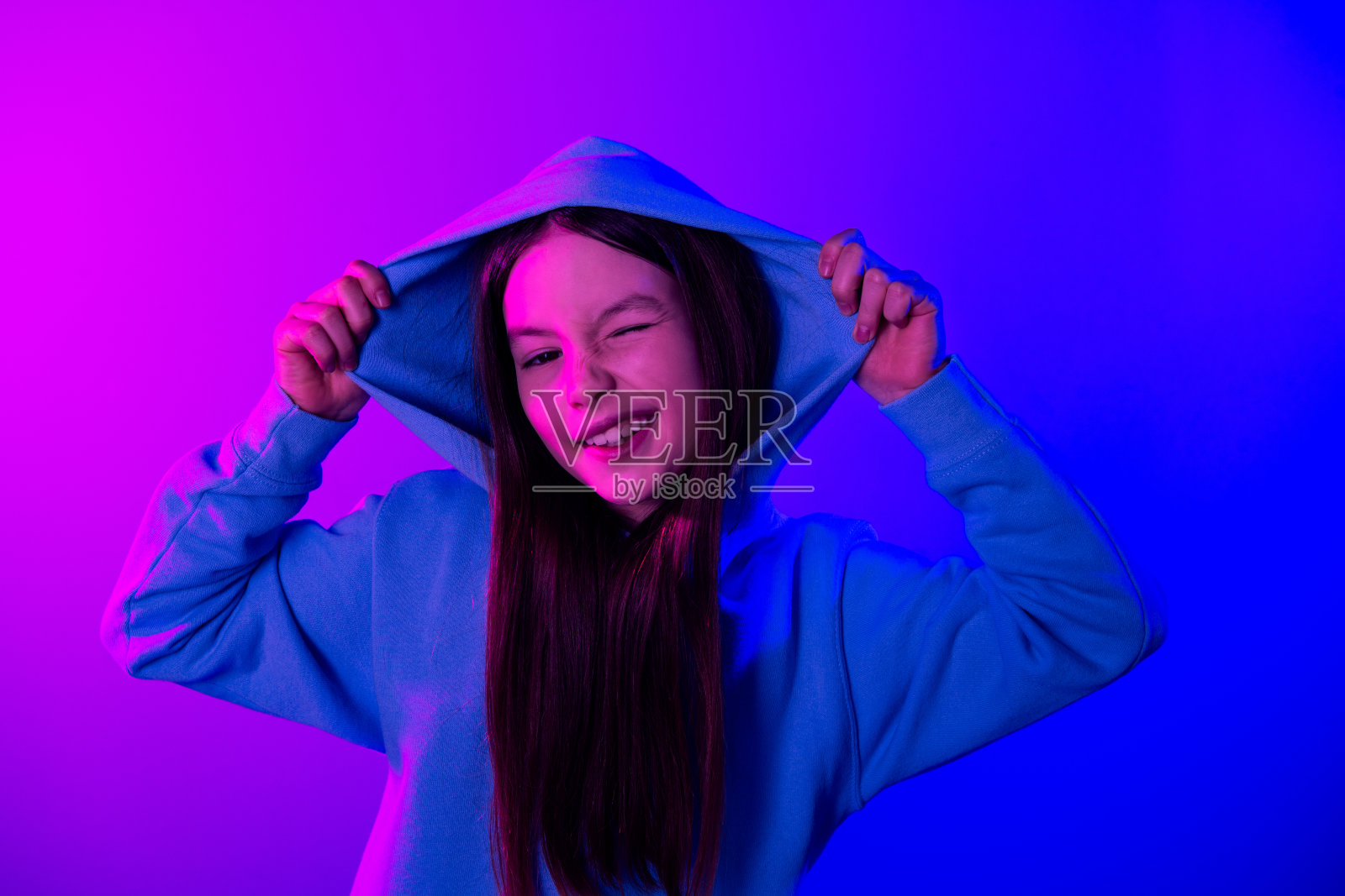 照片中开朗轻浮的小女士穿着运动衫手臂兜帽眨着眼睛空旷的空间孤立的霓虹紫色背景照片摄影图片