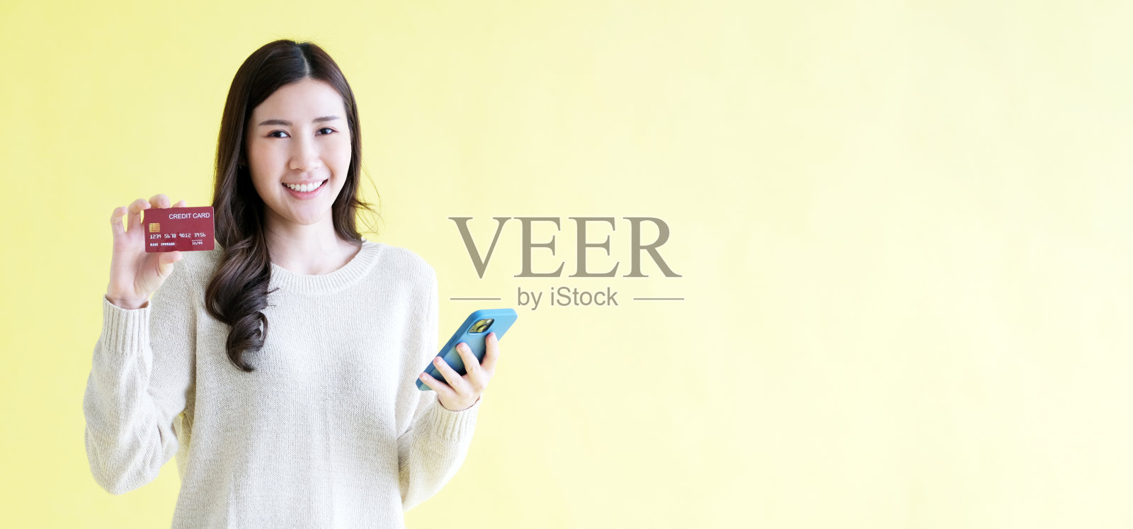 年轻的亚洲女子拿着手机和信用卡在网上购物，站在带有复制空间的孤立黄色背景上照片摄影图片