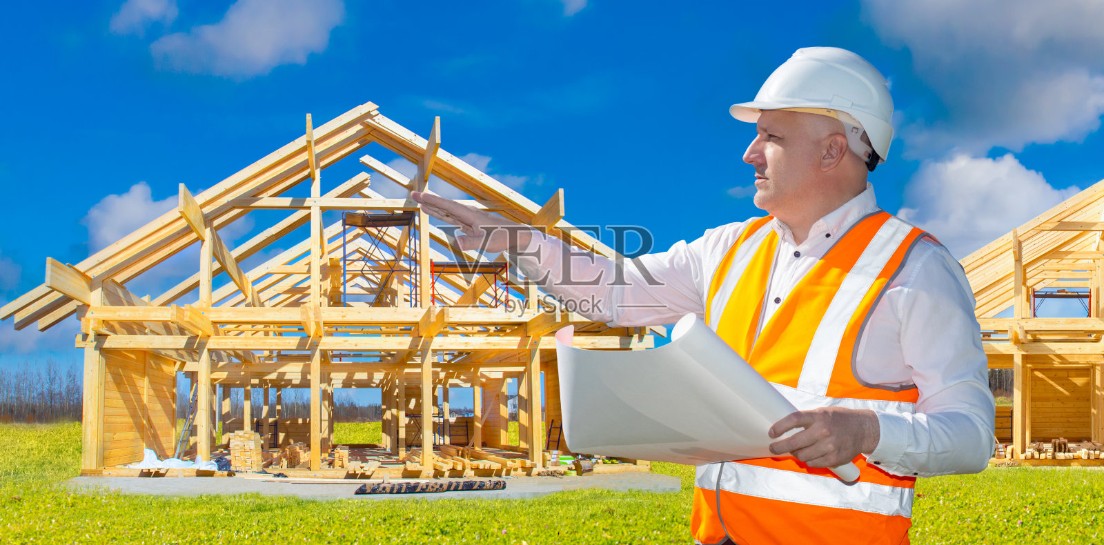 建筑公司领班。工头在未来建筑的地方展示他的手。人类在绿色的田野上。建筑局领班手里拿着图纸。戴头盔的建造者检查场地照片摄影图片