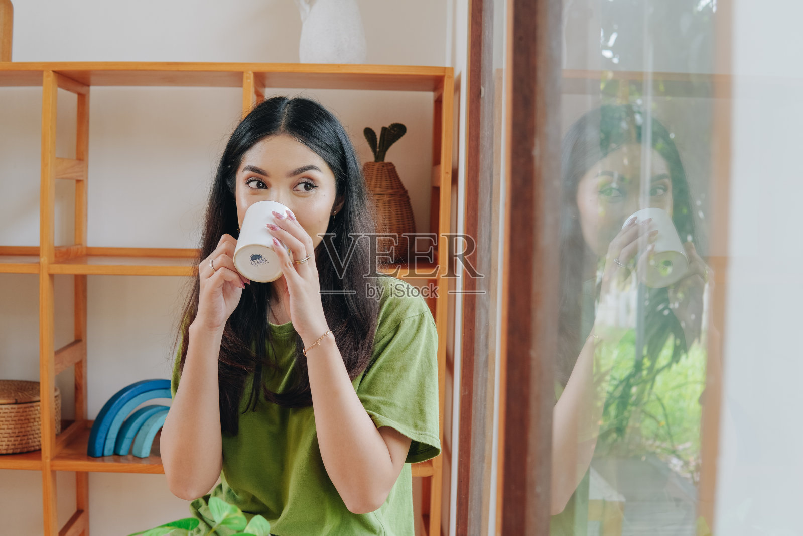 穿着绿色t恤的年轻亚洲女子正在喝水。照片摄影图片