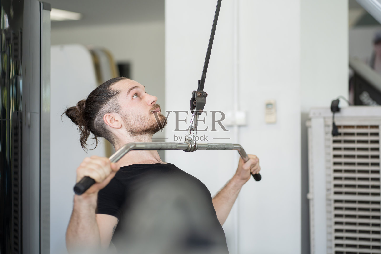 男子在健身房用上块的推力进行锻炼。男子在健身房努力训练。男子在坐式绳排机上举重。运动健身概念照片摄影图片