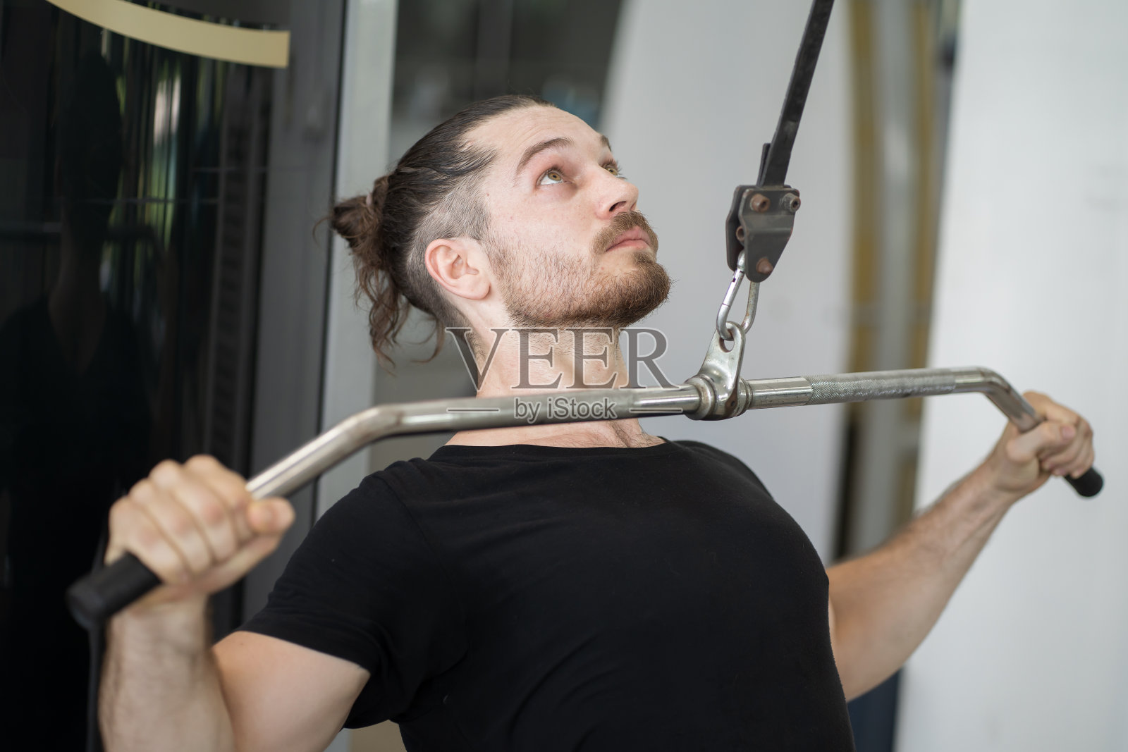 男子在健身房用上块的推力进行锻炼。男子在健身房努力训练。男子在坐式绳排机上举重。运动健身概念照片摄影图片