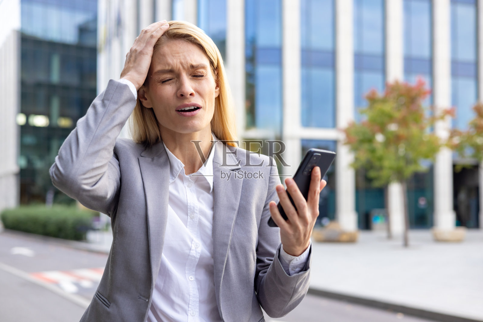 一位忧心忡忡的年轻女商人穿着西装站在外面的大街上，拿着手机，失望地用手捂着头，她得到了一个坏消息照片摄影图片