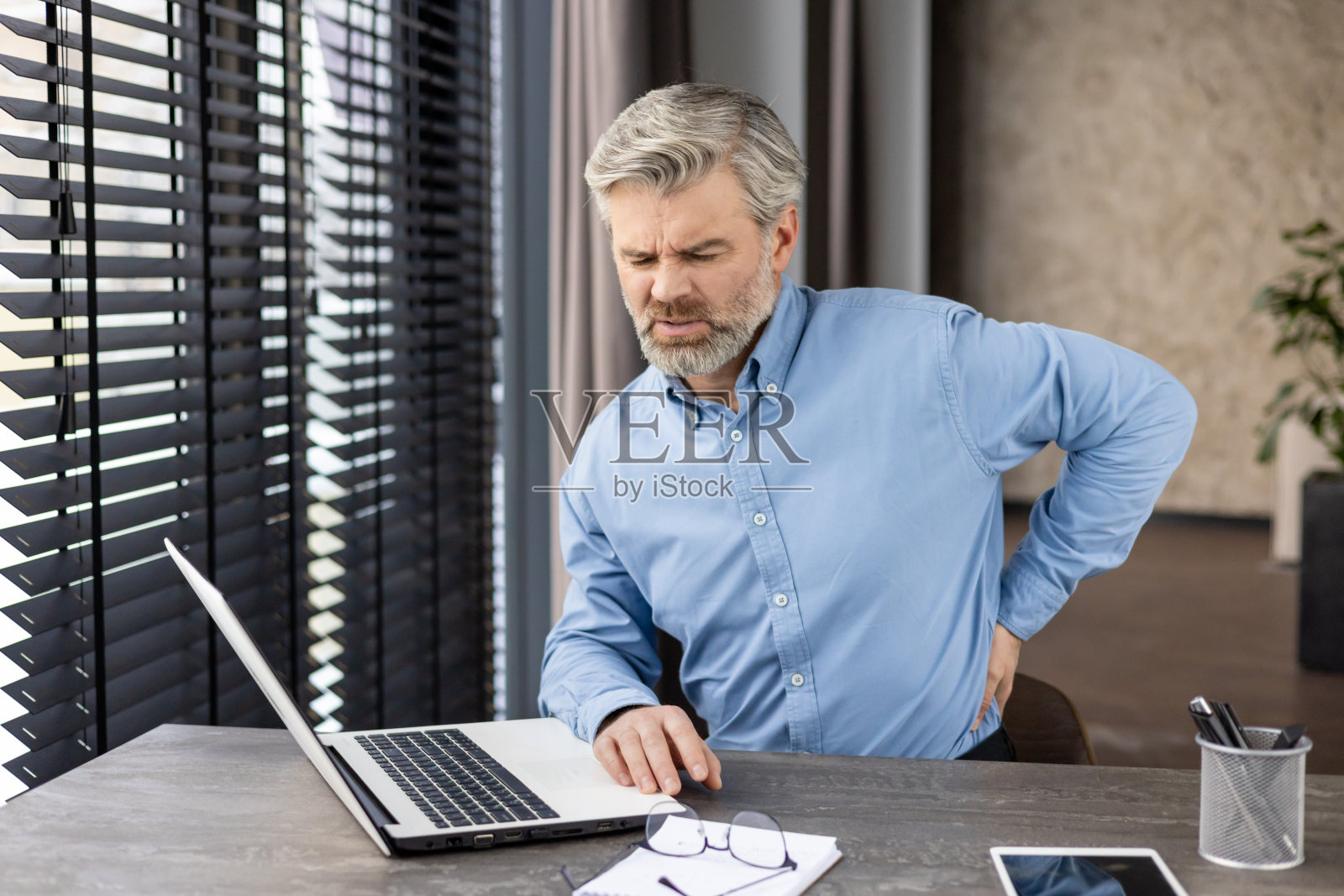 一名中年男子在办公工作站使用笔记本电脑时背部疼痛照片摄影图片