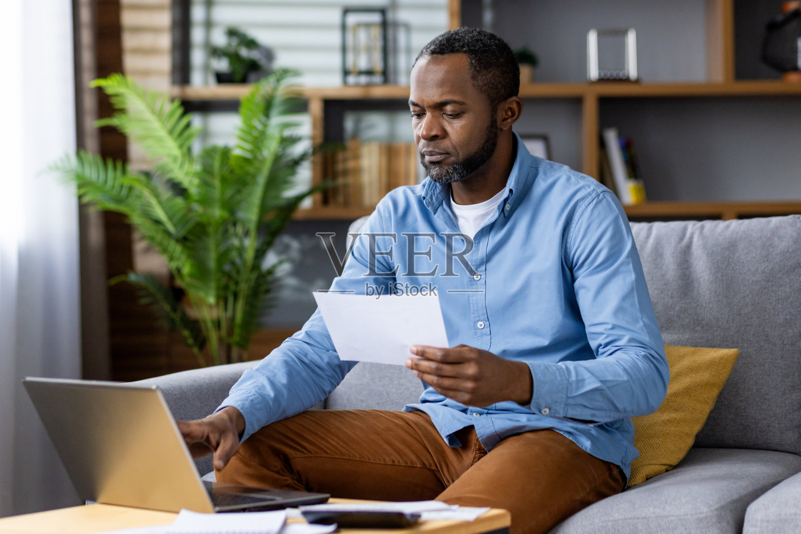一个男人在家工作，在舒适的客厅里查看文件，使用笔记本电脑，描绘了一个现代化的工作空间，专注于他的工作，奉献精神和效率照片摄影图片