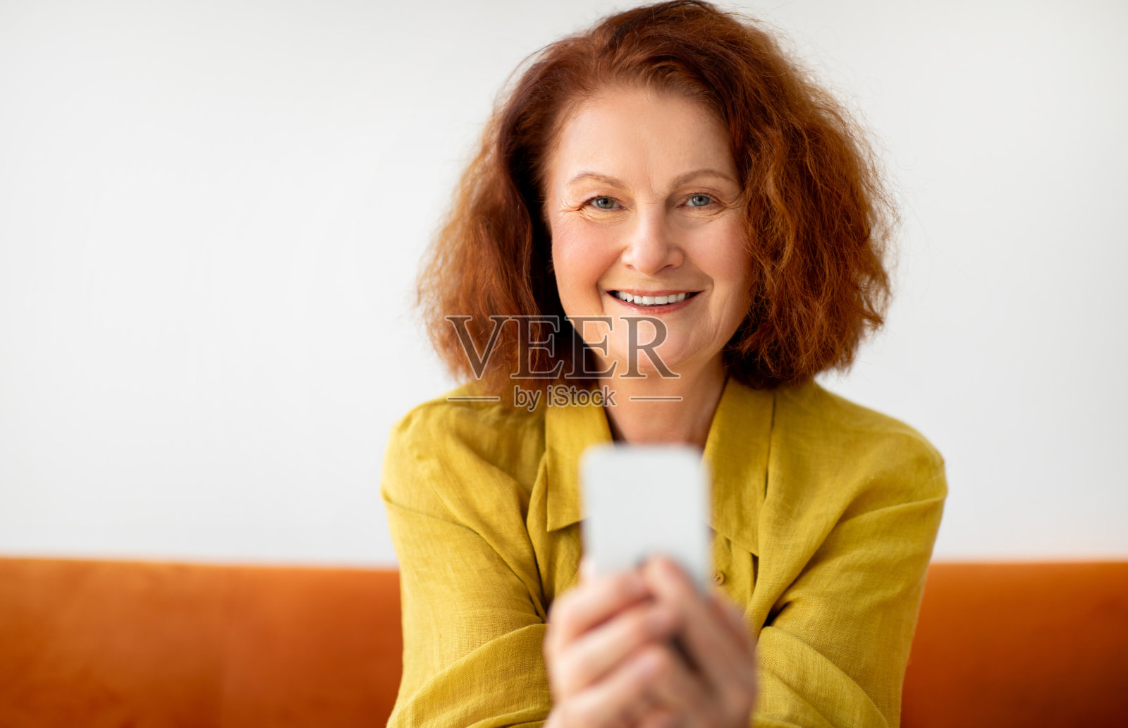 手拿智能手机坐在家里沙发上微笑的老年妇女照片摄影图片