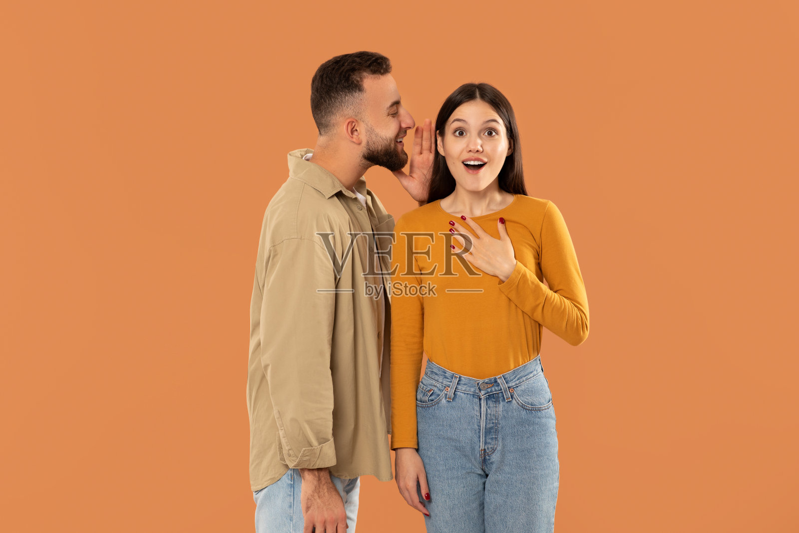 在工作室里，橙色背景下，男人对女人耳语照片摄影图片