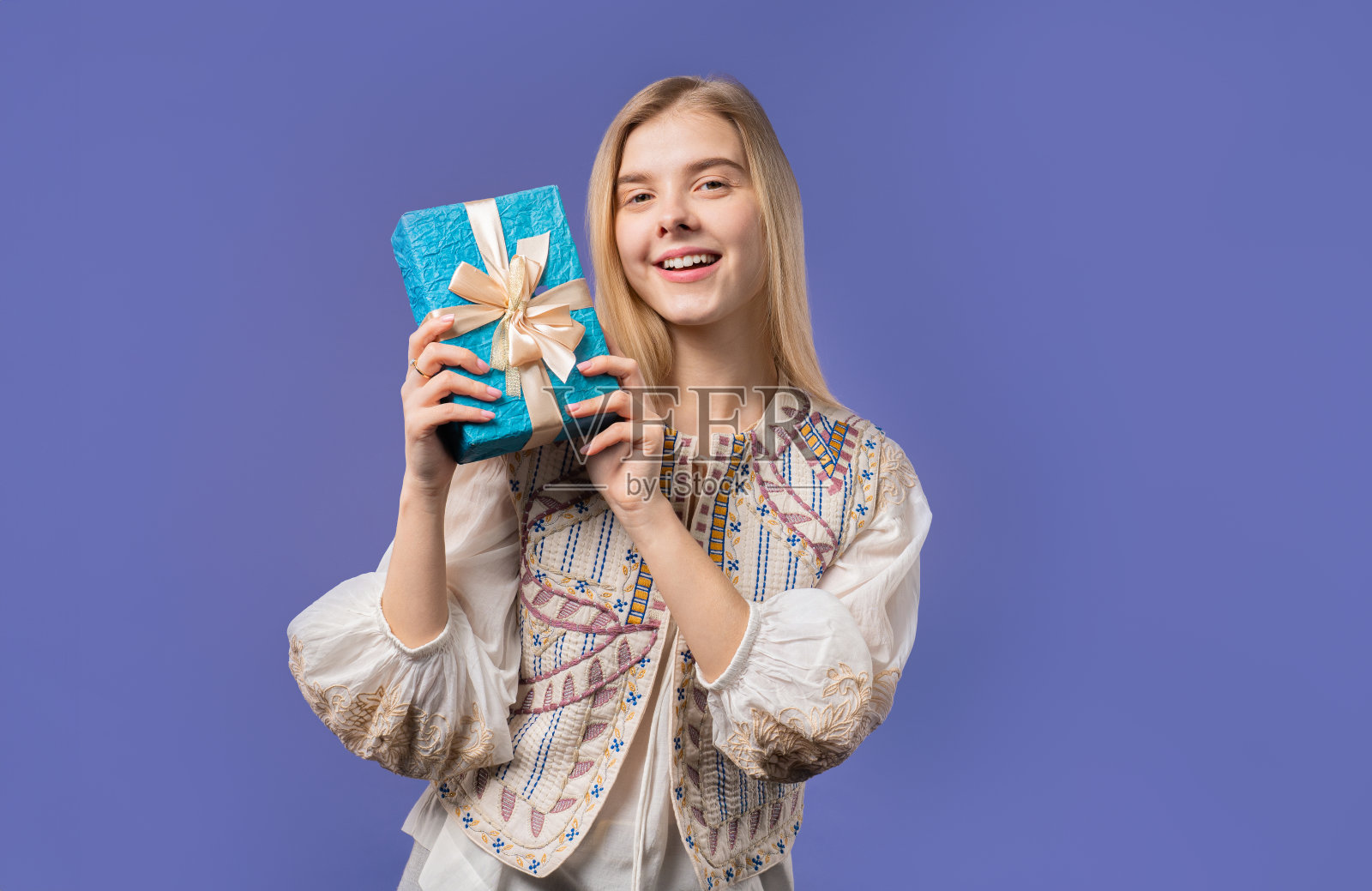 快乐少女带礼盒，紫罗兰墙。微笑着，对里面的东西感兴趣照片摄影图片