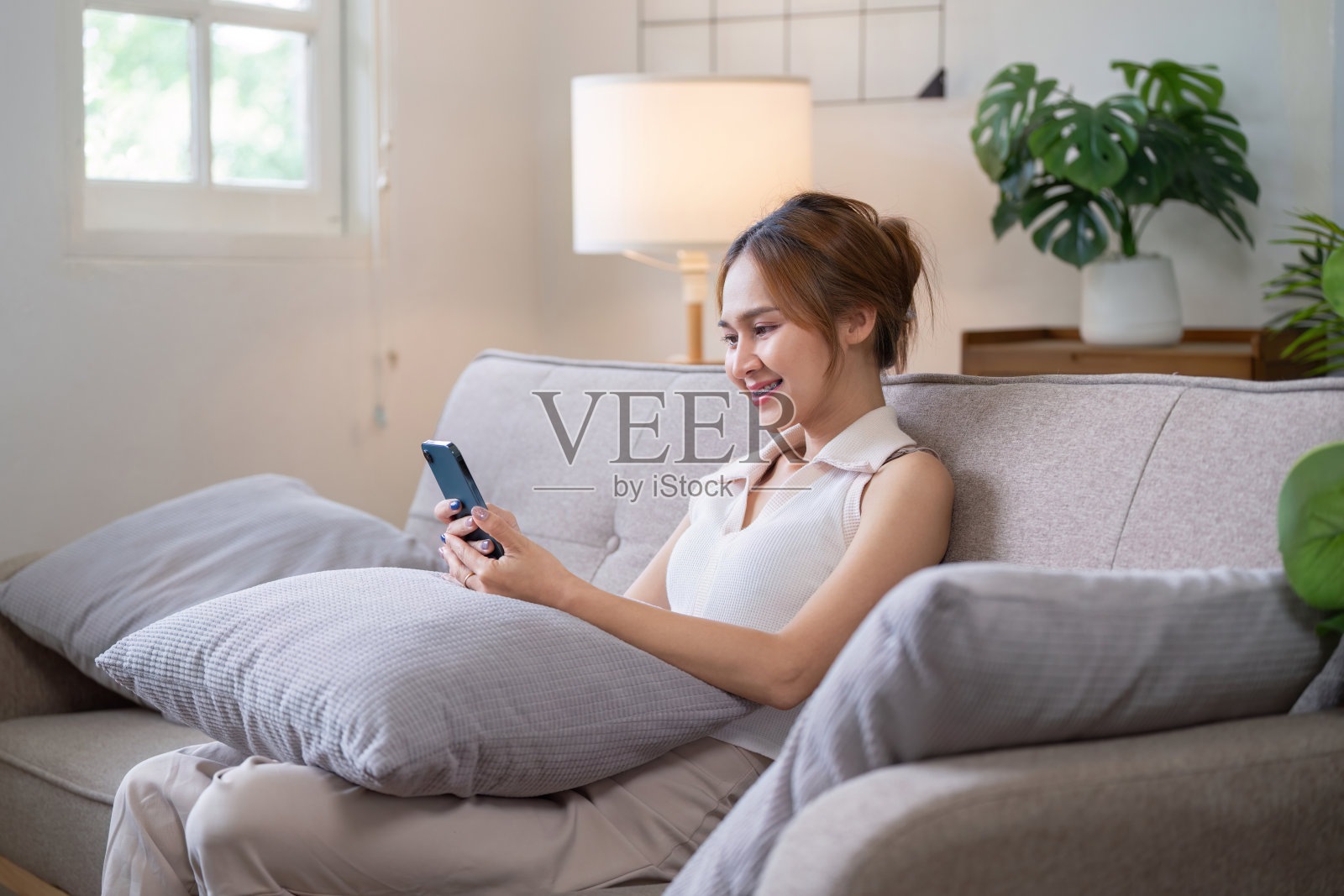 年轻女子在沙发上放松，在舒适的客厅里用智能手机玩社交媒体照片摄影图片