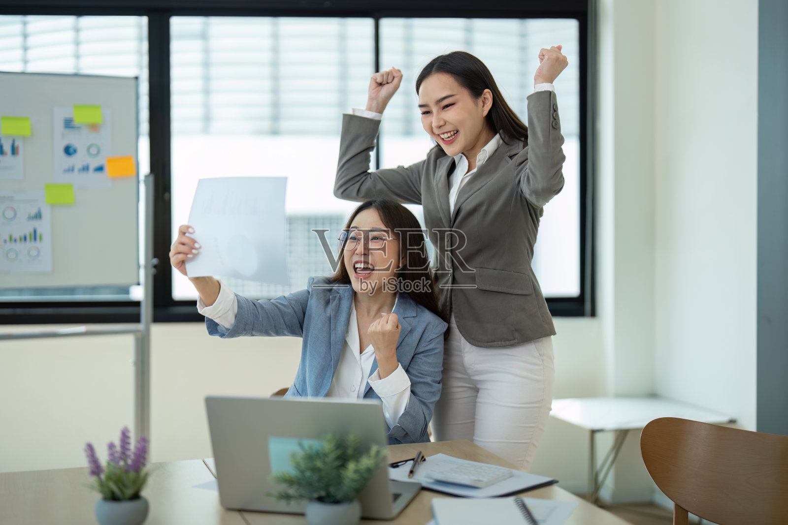 两个快乐的女商人用文档和笔记本电脑庆祝现代办公室的成功照片摄影图片