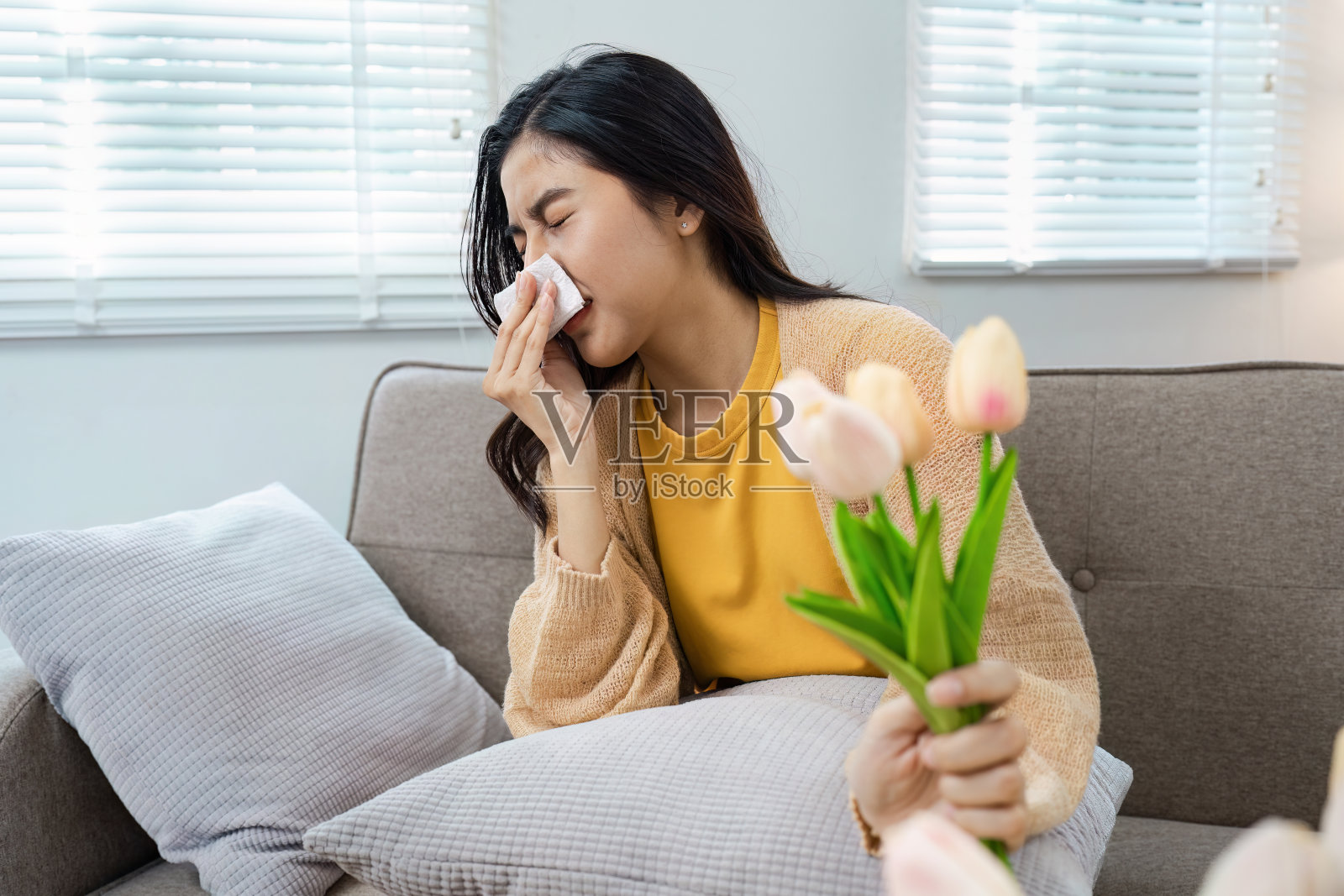 年轻女子在明亮的客厅里捧着郁金香时因花粉过敏而打喷嚏照片摄影图片