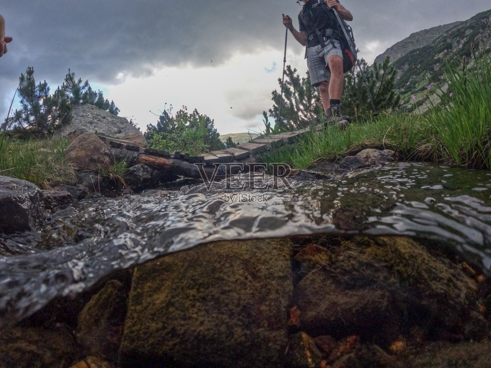 穿越山间河流的男性徒步旅行者照片摄影图片