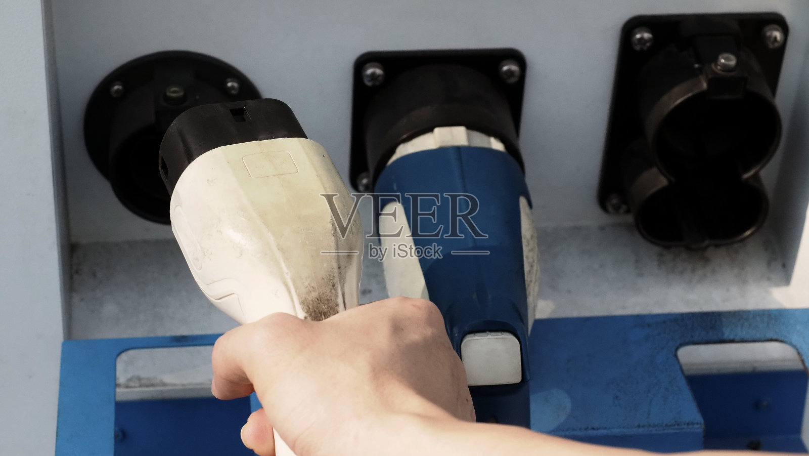 电动车司机手持电池充电器插头。手持电动汽车充电插头在相机前，室外背景模糊。可持续能源充电站背景照片摄影图片