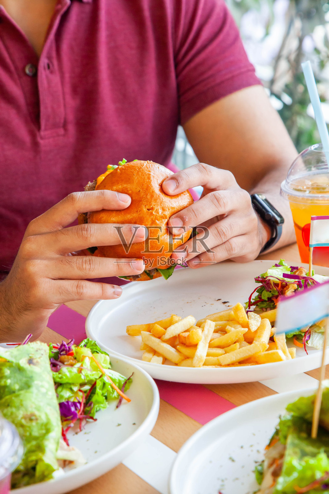 在咖啡馆里，男孩拿着一个装在奶油面包里的蜂蜜鸡肉汉堡，配上炸薯条和沙拉。照片摄影图片