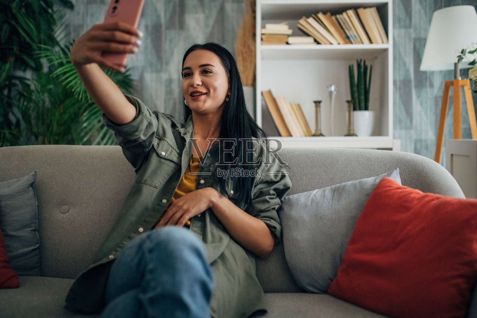坐在沙发上用手机自拍的女人。照片摄影图片